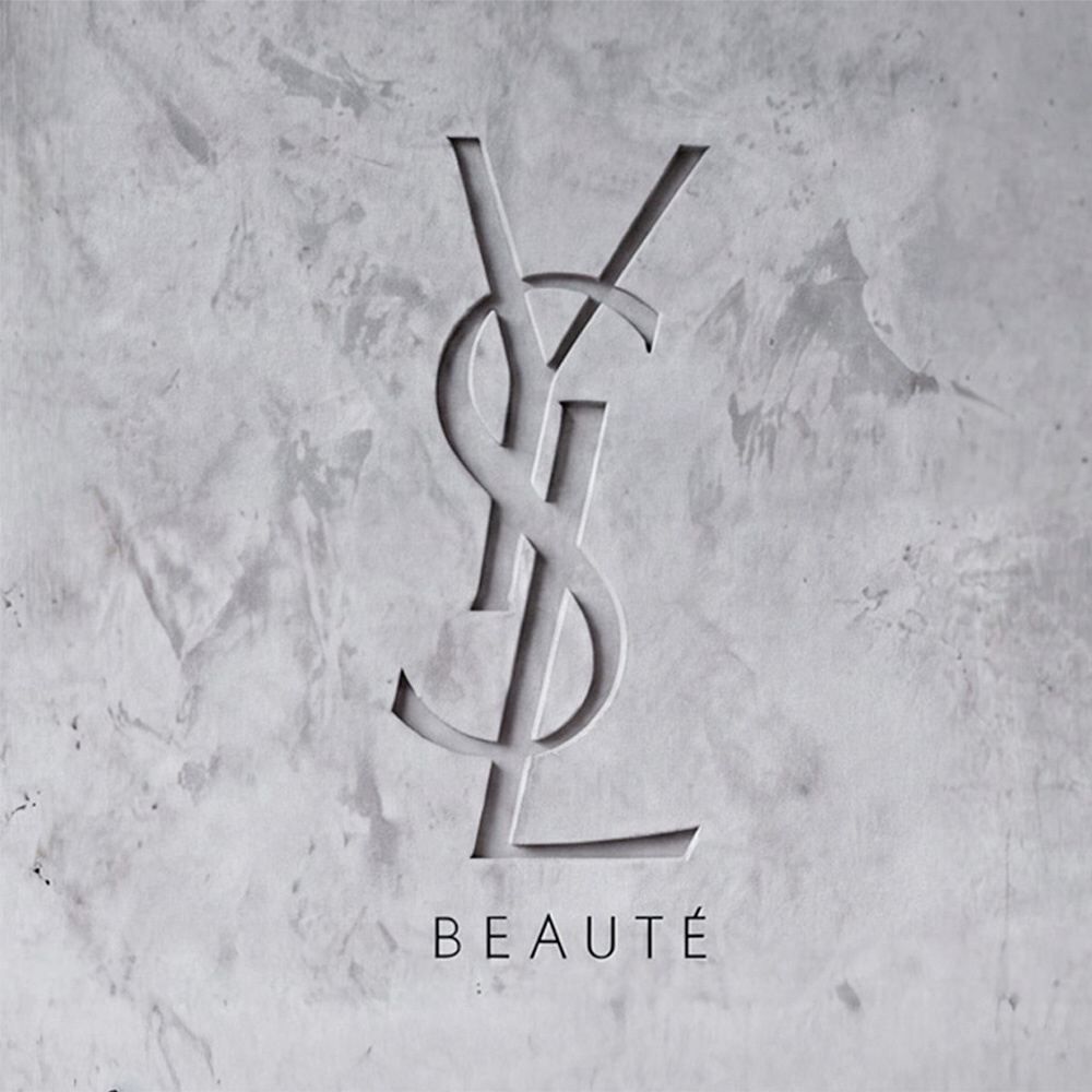 YSL BEAUTE logo carved into a textured grey concrete wall.​