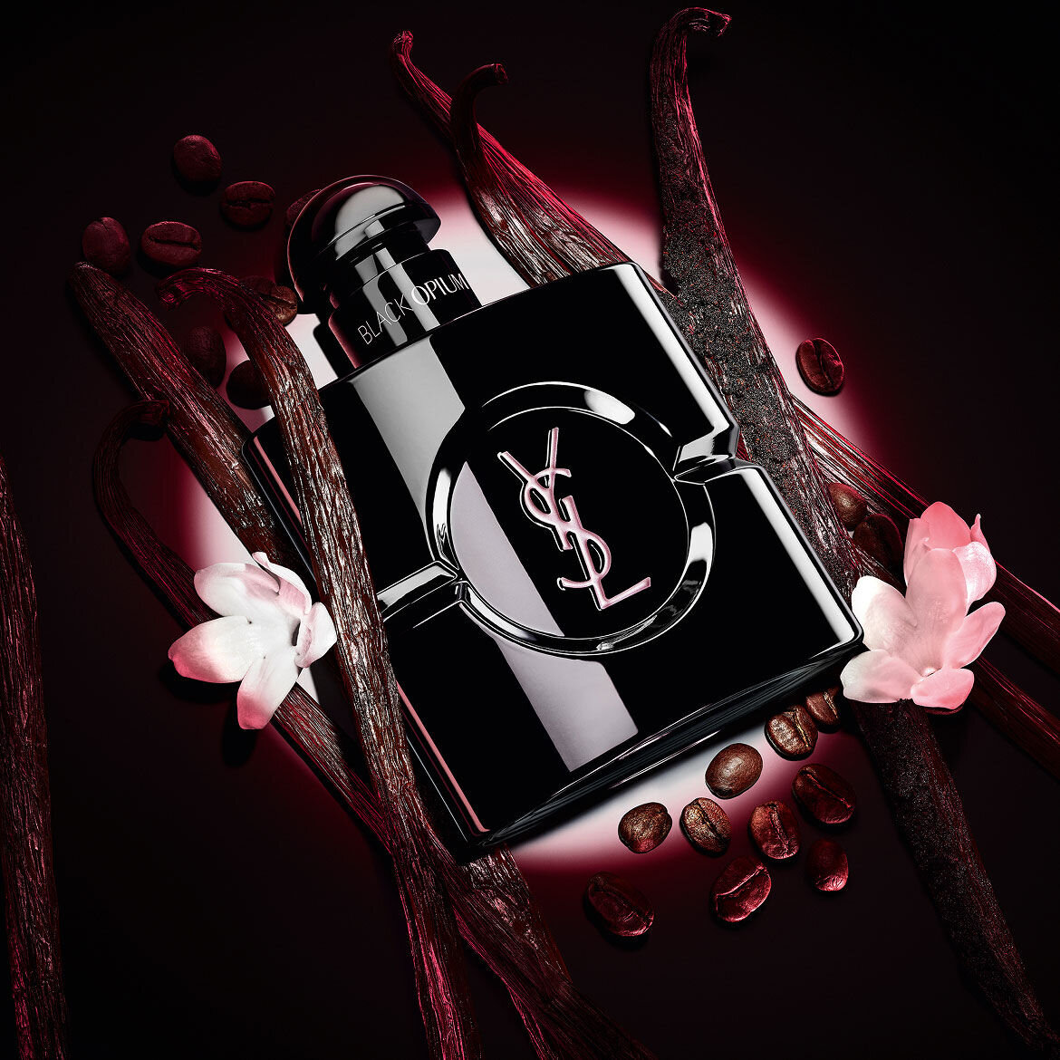 Flacon Black Opium Le Parfum noir brillant, entoure de gousses de vanille sombre et de jasmin blanc.