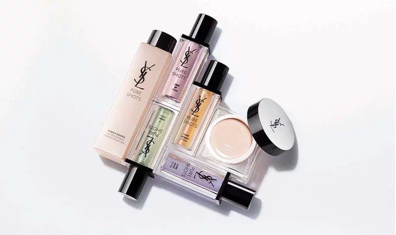A flat lay of various YSL beauty products, including foundations, serums, and creams, arranged artistically on a clean, light background.