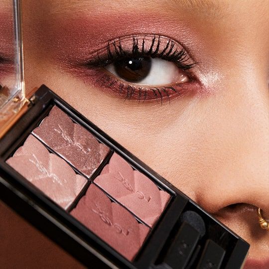 Close-up of a woman's eye with soft, shimmering eyeshadow in shades of pink, showcasing a compact of makeup featuring complementary colors.