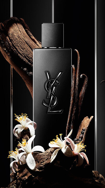 Flacon de parfum YSL noir entoure de bois, de gousses de vanille et de fleurs blanches.