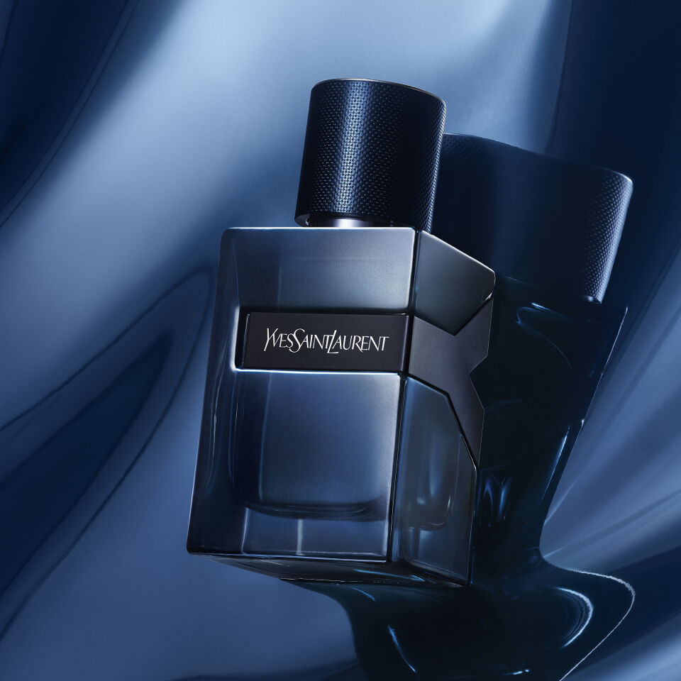 A stylish bottle of Yves Saint Laurent fragrance "Y" displayed alongside its box and a sample vial, resting on a glossy black guitar.
