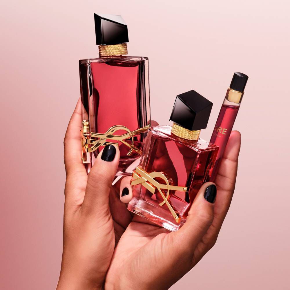 Hande halten zwei rote YSL-Parfumflakons und ein Reisespray