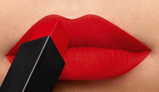 Close-up of vibrant red lips with a lipstick tube held against them.