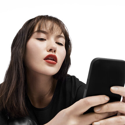 Eine Frau mit langen, dunklen Haaren und rotem Lippenstift, die auf ein Smartphone schaut.