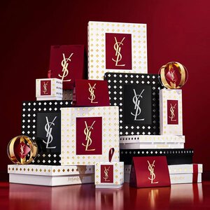 Coffrets cadeaux de la collection de fetes Yves Saint Laurent et produits de beaute de luxe sur fond rouge festif.