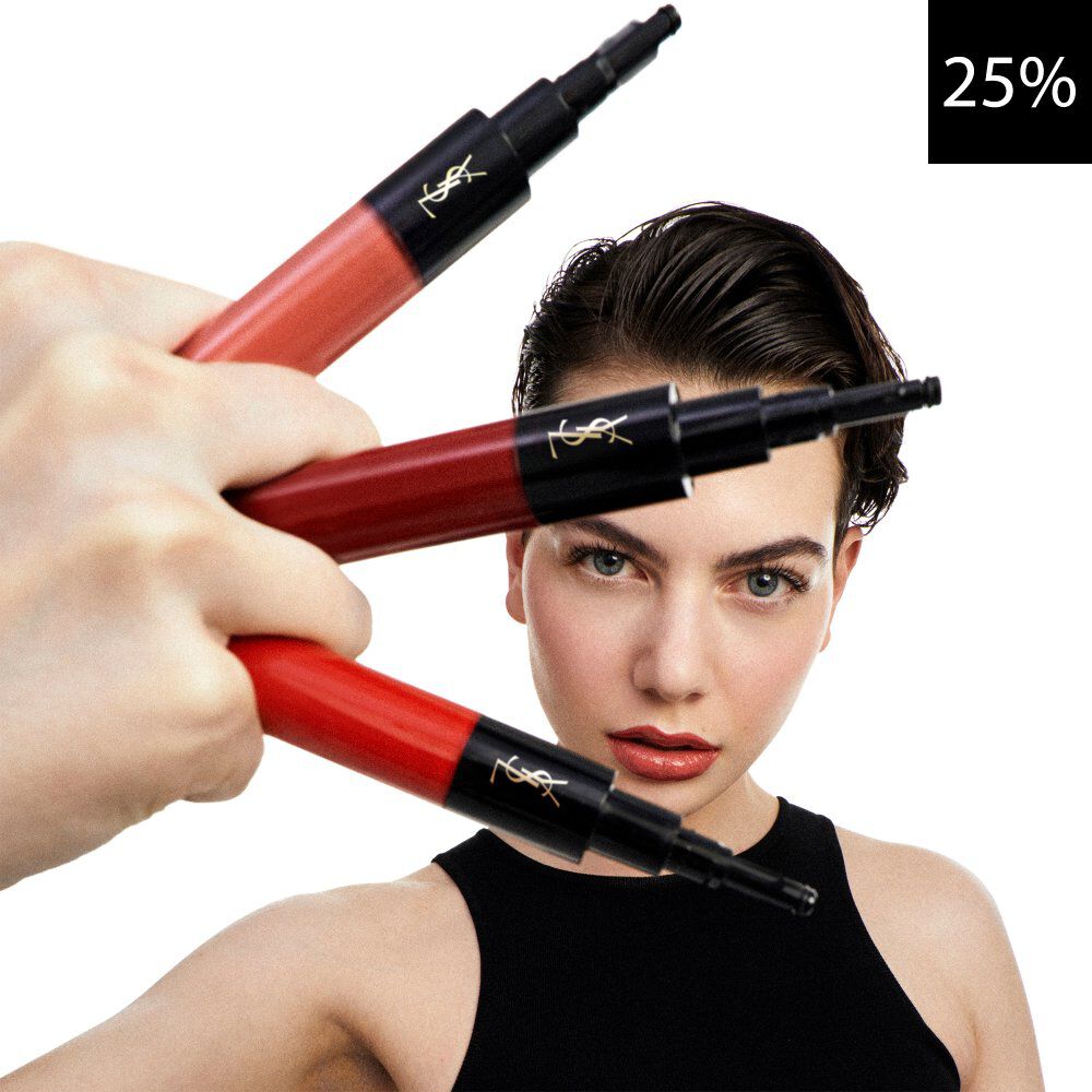 Ein Nahaufnahmebild, das ein nach vorne blickendes Model zeigt, wahrend eine Hand drei YSL Flussiglippenprodukte in Rot- und Koralltonen halt. Ein schwarzes Quadrat mit weißem Text '25%' ist in der oberen rechten Ecke sichtbar und weist auf einen Rabatt hin.