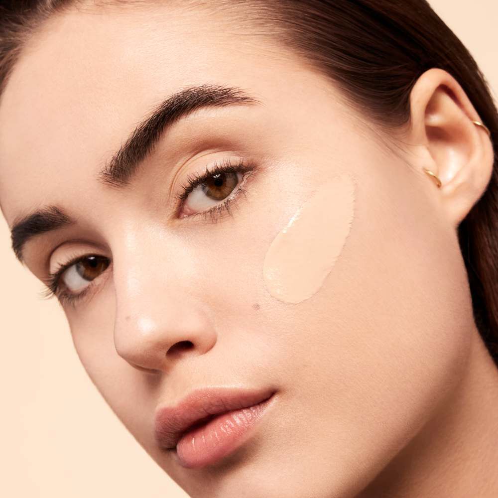A close-up of a person's face with a smooth, neutral makeup applied to one cheek, highlighting their natural features and skin tone.