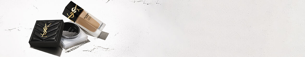 A close-up of a woman's face with striking blue and orange eye makeup, showcasing a bold and artistic look. She has dark hair and is wearing elegant earrings. The background is a soft, neutral color.