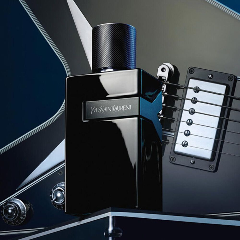A sleek black perfume bottle placed on a blue electric guitar, featuring the label "Yves Saint Laurent."