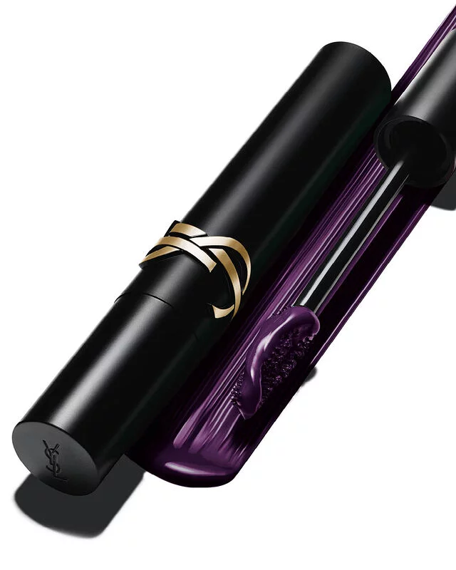 Nahaufnahme einer schwarzen Mascara-Tube mit goldenem Logo neben einer Burste mit tiefvioletter Textur.