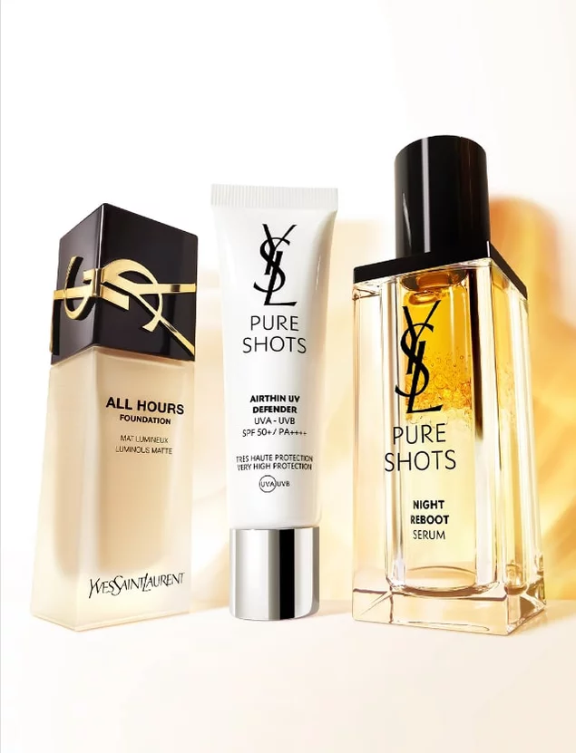 Three YSL beauty products: a foundation bottle, a moisturizer tube, and a night serum, elegantly displayed against a soft gradient background.