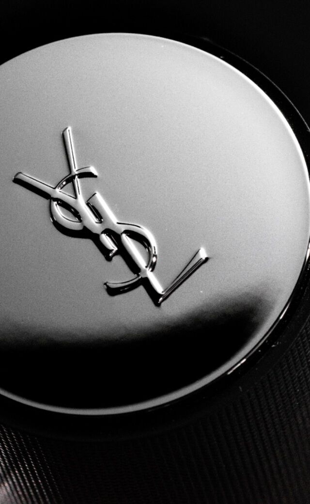 Close-up of a YSL perfume bottle cap featuring the brand's logo on a black background.