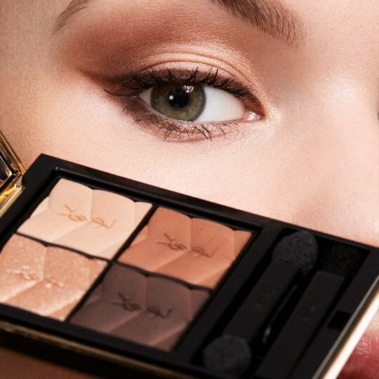 Close-up of a woman's eye with subtle eyeshadow applied, holding a palette of neutral tones featuring four shades.