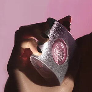 Femme tenant un flacon de parfum sur fond rose.