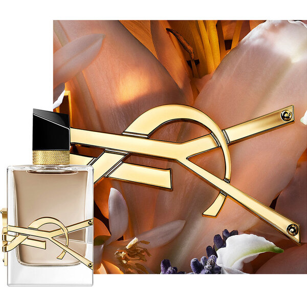 Flacon LIBRE FLOWERS & FLAMES encadre de petales cremeux et du logo YSL dore, baigne d’une lumiere chaude.