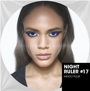 Un portrait rapproche en couleur d'une femme aux longs cheveux bruns raides et au teint clair. Ses yeux sont intensement maquilles avec un eyeliner bleu electrique vibrant et un fard a paupieres bronze. Ses levres sont naturelles et brillantes. En bas a droite de l'image circulaire, une incrustation rectangulaire noire indique "NIGHT RULER #17" et "INDIGO PULSE", suggerant une collection ou une ambiance energique et audacieuse, comme un titre de morceau de musique.