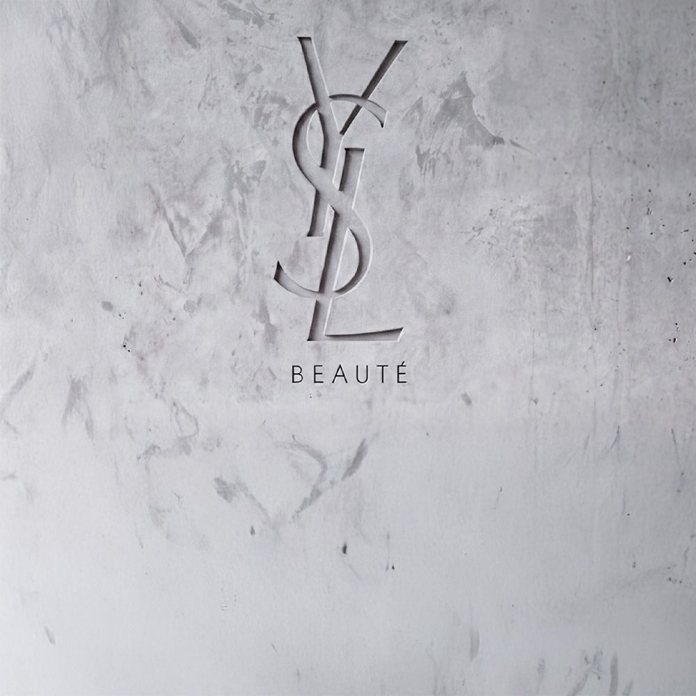 In eine strukturierte graue Betonwand graviertes YSL BEAUTE Logo.