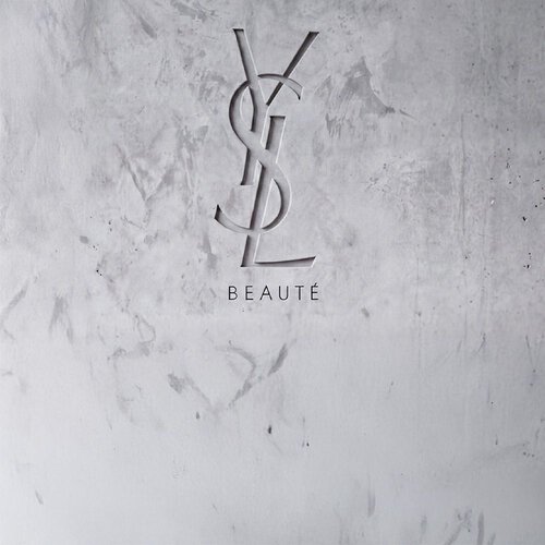 In eine strukturierte graue Betonwand graviertes YSL BEAUTE Logo.