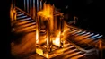Une bouteille de parfum rectangulaire transparente est montree en train d'etre chauffee par des flammes, probablement dans le cadre d'un processus de fabrication ou de traitement du verre.
