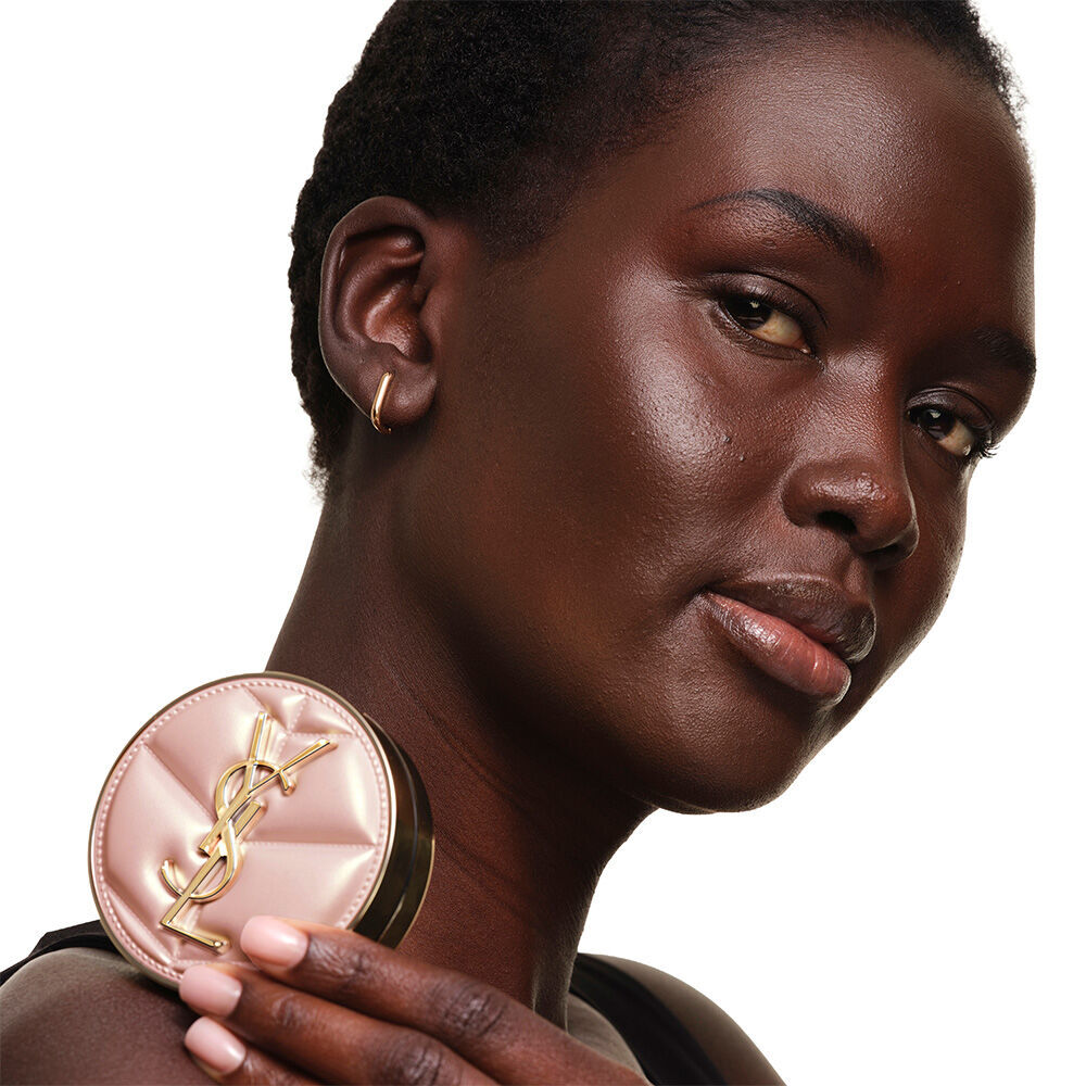 Ein Modell mit glatter, strahlender Haut halt das pinke YSL SKIN AFFAIR CUSHION FOUNDATION, um einen naturlichen, leuchtenden und makellosen Teint zu prasentieren.