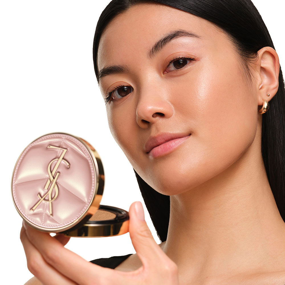 Model mit glatter, strahlender Haut, die das pinke YSL SKIN AFFAIR CUSHION FOUNDATION halt und ein naturlich leuchtendes, makelloses Hautbild prasentiert.