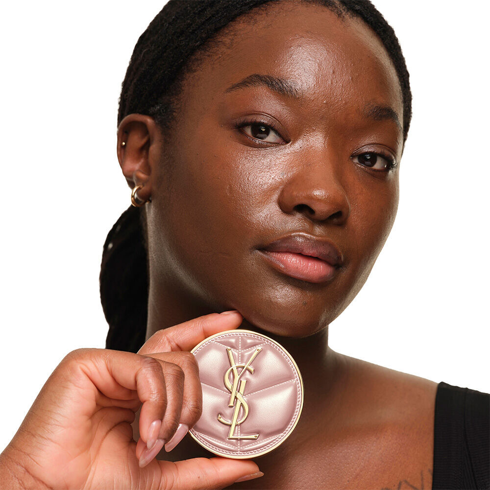 Model mit glatter, strahlender Haut, die das pinke YSL SKIN AFFAIR CUSHION FOUNDATION halt, um ein naturliches, leuchtendes und makelloses Hautbild zu prasentieren.