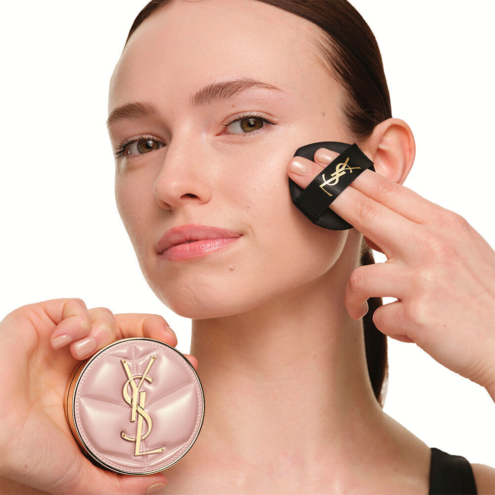 Model mit einem glatten, strahlenden Teint, der das pinke YSL SKIN AFFAIR CUSHION FOUNDATION halt, um eine naturlich leuchtende, makellose Haut zu prasentieren.