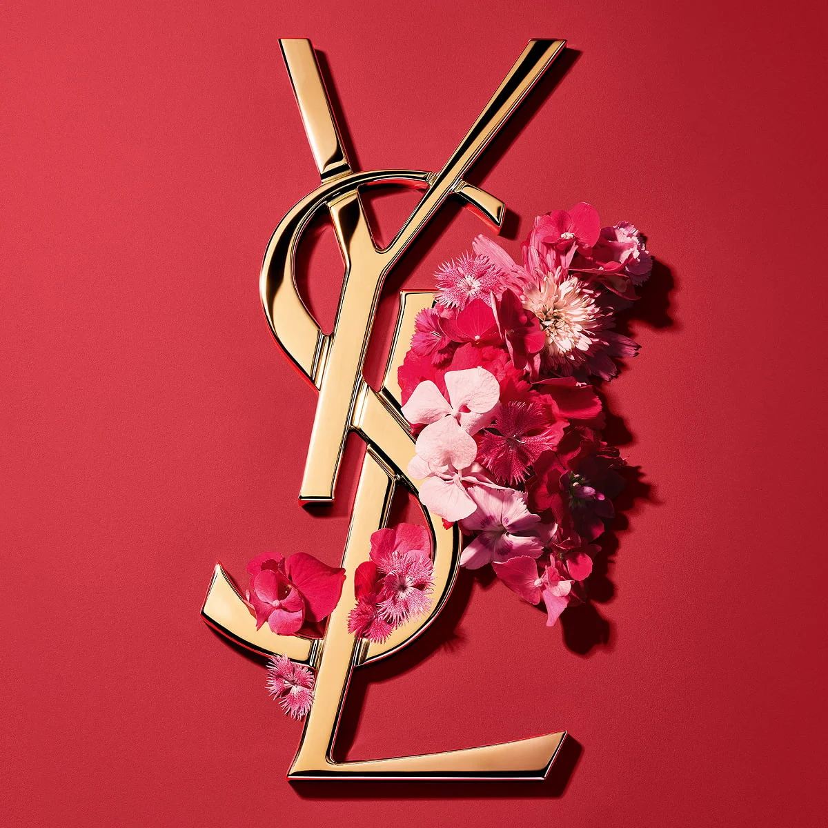 Goldenes YSL Cassandre-Logo, geschmückt mit leuchtend rosafarbenen Frühlingsblumen, auf einem rosafarbenen Hintergrund.
