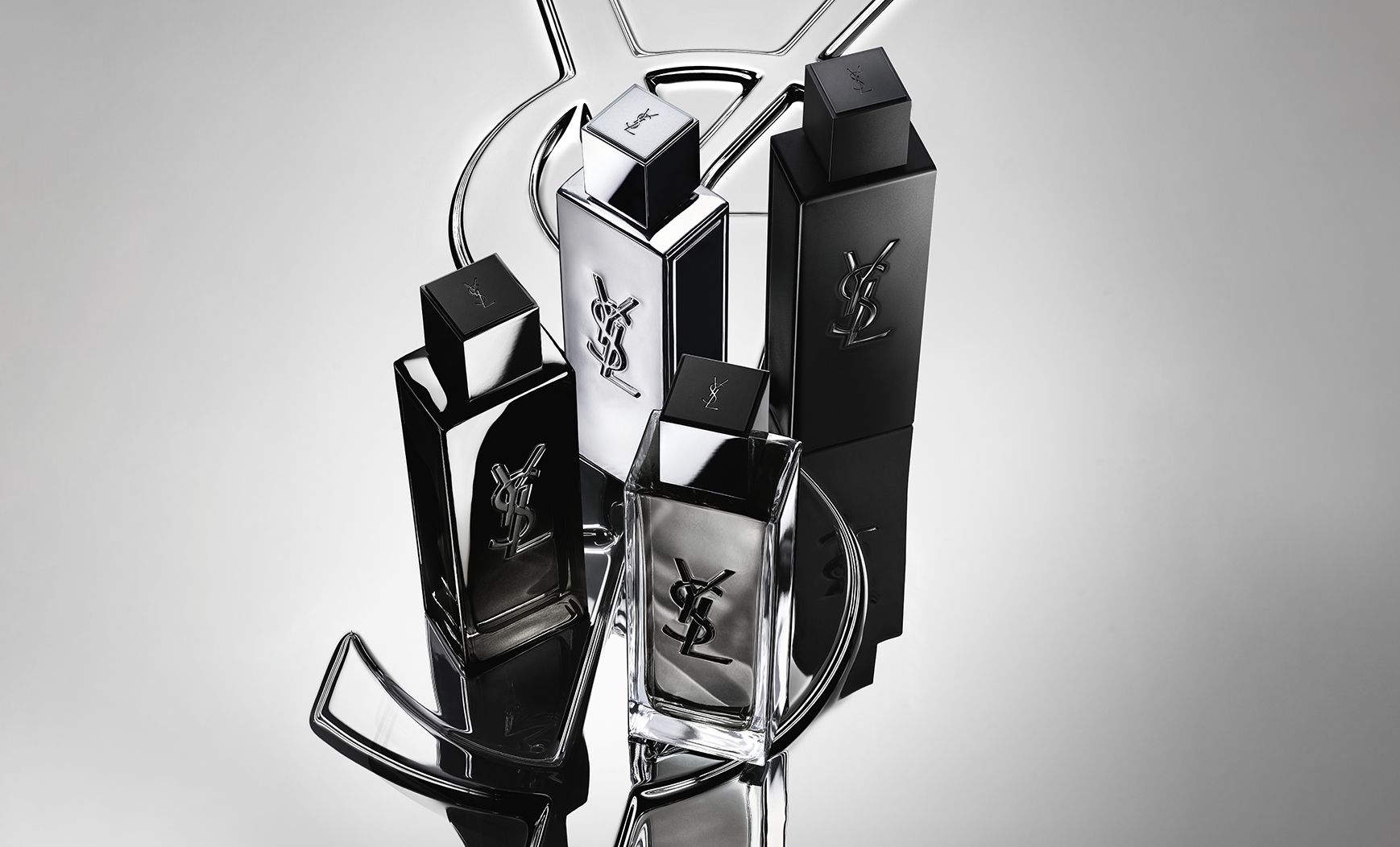 Gruppenaufnahme der gesamten MYSLF Duftreihe mit Flakons, die auf einem großen YSL-Cassandre-Logo mit spiegelndem Reflexeffekt stehen.