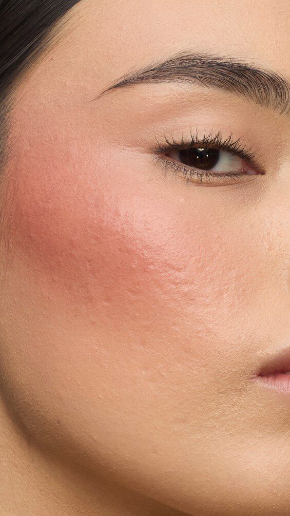 Gros plan sur la joue d’un modèle portant la routine Make Me Blush : Poudre #37 Peachy Nude superposée à la Crème #90 Toffee Temptation pour un éclat baigné de soleil.