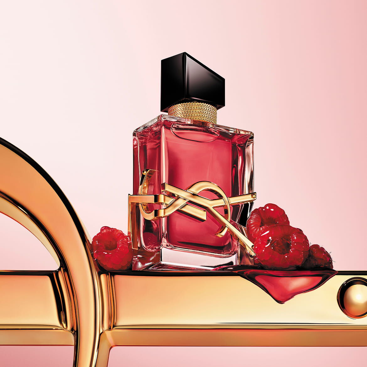 Flacon de parfum YSL rouge avec logo doré, sur une surface dorée avec des framboises.
