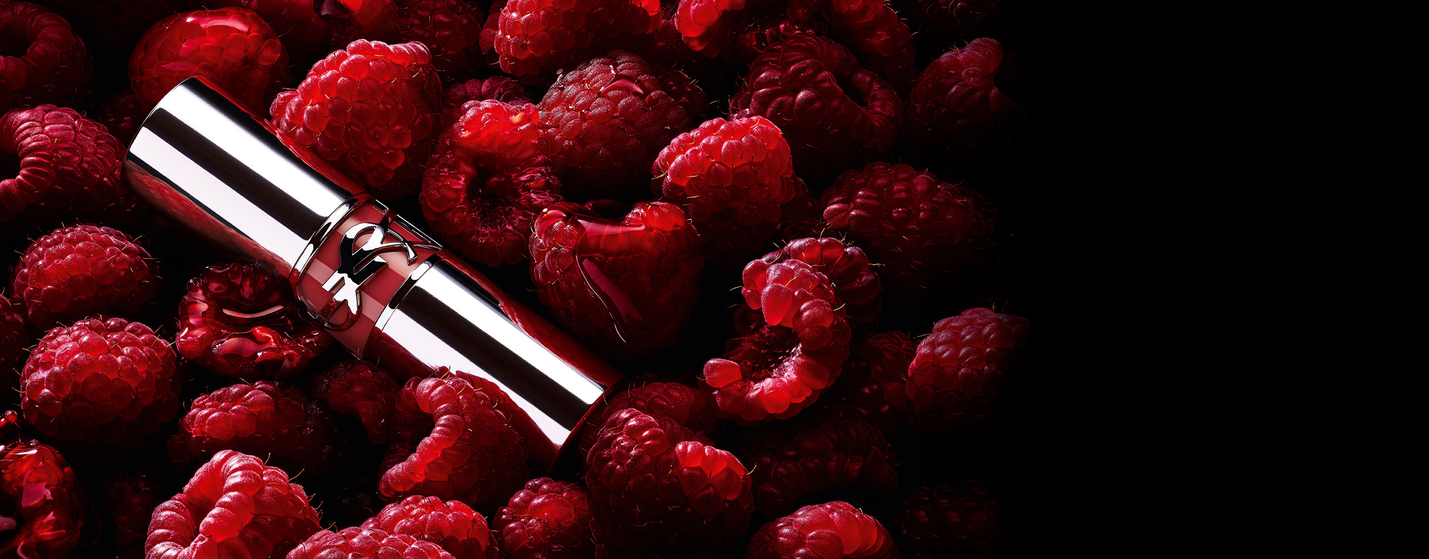 YSL LOVESHINE Berry Crush Lippenstift, silberne Hülse mit beerenfarbenem YSL-Logo, gebettet zwischen frischen Himbeeren.