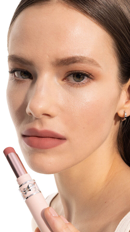 Model Jade wearing YSL LOVENUDE Lip Blusher in Shade 2, holding the product near her rosy nude lips.