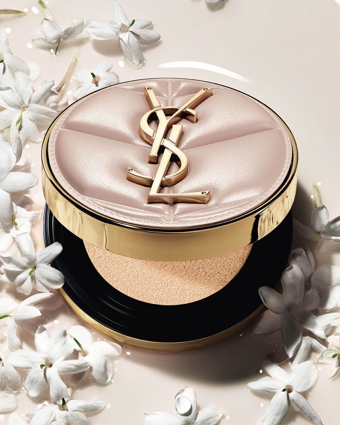 Nahaufnahme des YSL SKIN AFFAIR SOFT GLOW CUSHION in einem Pool aus flüssigem Make-up und Jasminblüten. Strahlendes, sinnliches Finish.