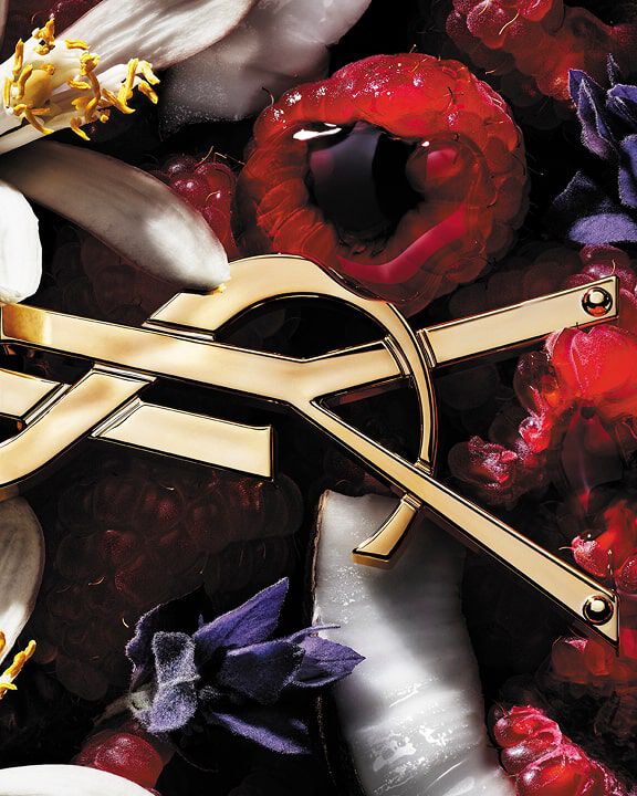 Logo YSL entouré de framboises, de fleurs blanches et violettes et de noix de coco.