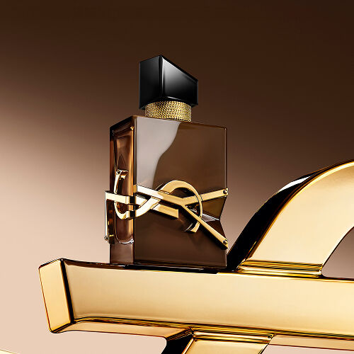 Glasierter brauner Libre Santal Couture Flakon, der das Licht reflektiert, platziert auf einer großen goldenen YSL Cassandre.