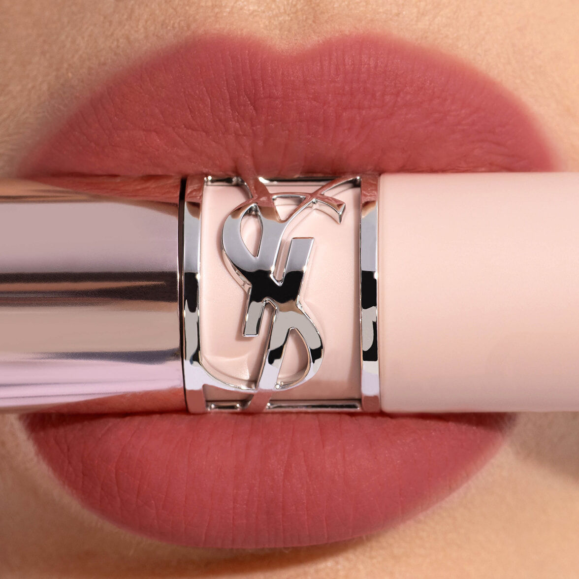 Close-up lips wearing YSL LOVENUDE LIP BLUSHER in Shade 4 with a pale pink YSL lipstick tube and silver Cassandre ring.