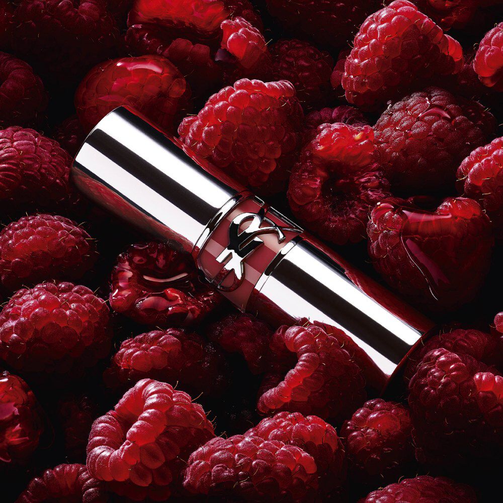 YSL LOVESHINE Berry Crush Lippenstift, silberne Hülse mit beerenfarbenem YSL-Logo, gebettet in frischen Himbeeren.