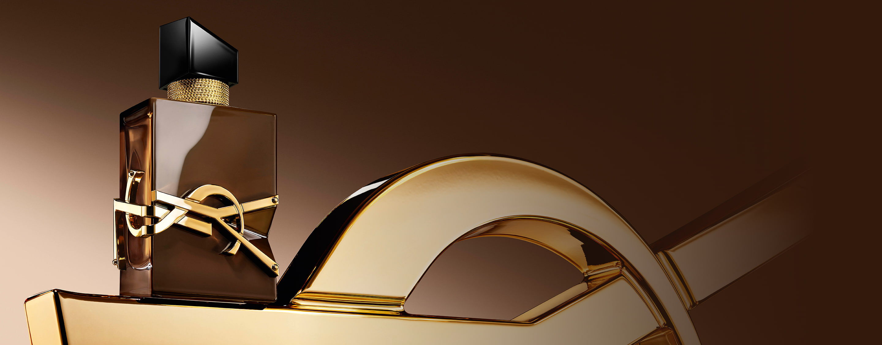 Glasierter brauner Libre Santal Couture-Flakon, der das Licht reflektiert, auf einer grossen goldenen YSL-Cassandre platziert.