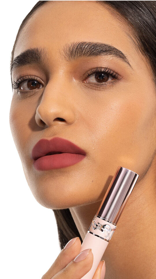 Model Merna wearing YSL LOVENUDE Lip Blusher in Shade 4, holding the product near her rosy nude lips.